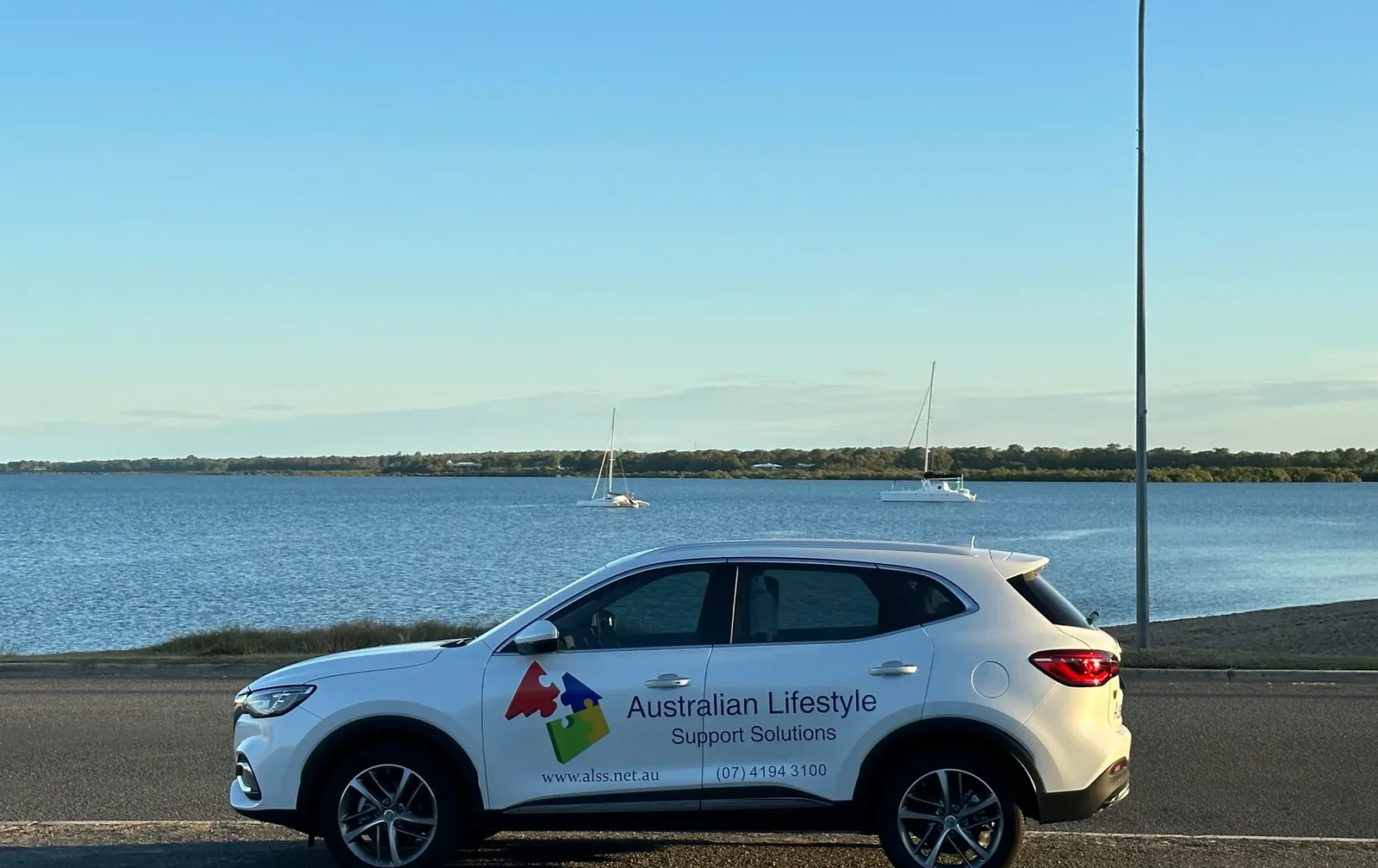 An Australian Lifestyle Support Solutions branded vehicle parked by the waterfront at dusk.
